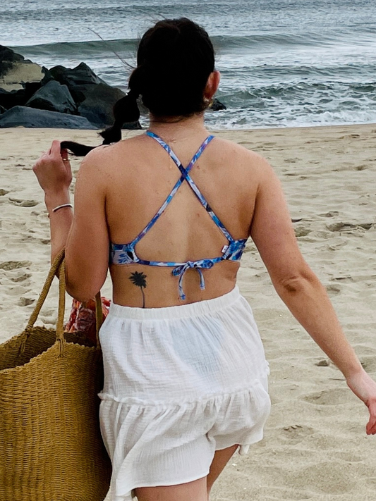 woman on the beach in a white skirt and a cross back blue floral bikini top