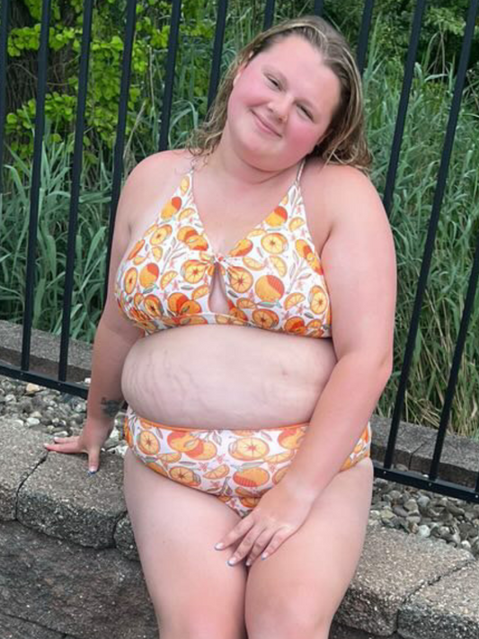 plus sized woman in supportive orange print peek a boo, crossed back top and matching high waisted bottoms