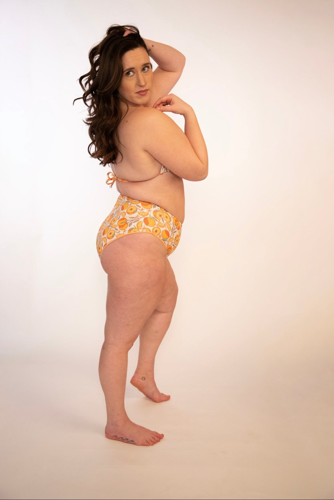 side view of curvy girl in orange print high waisted, high hip, reversible bikini bottoms and matching top