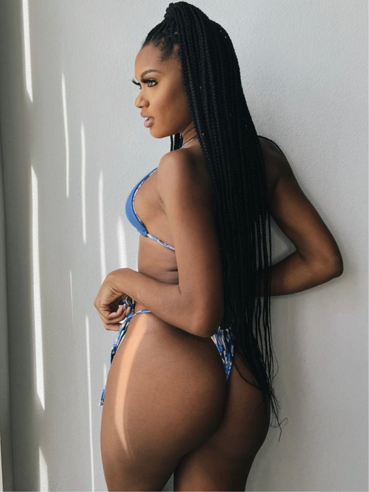 black woman with long braids wearing a reversible blue triangle top and blue floral thong bikini bottoms from behind