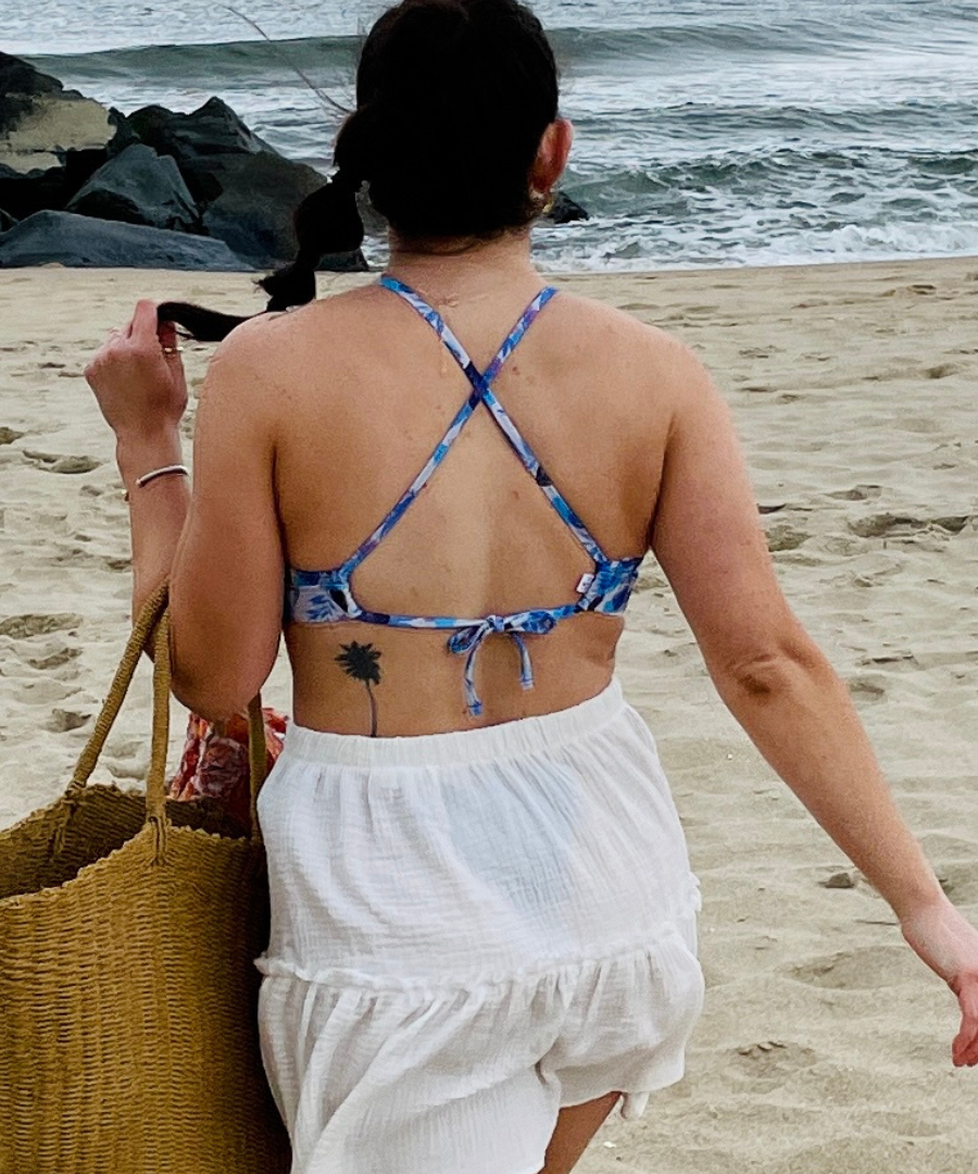 woman on the beach in a white skirt and a cross back blue floral bikini top