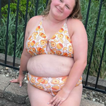 plus sized woman in supportive orange print peek a boo, crossed back top and matching high waisted bottoms