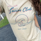close up of a woman in a short sleeve, sand colored tshirt with a graphic of a wave in front of a circle with the words "Portside swim club" above it
