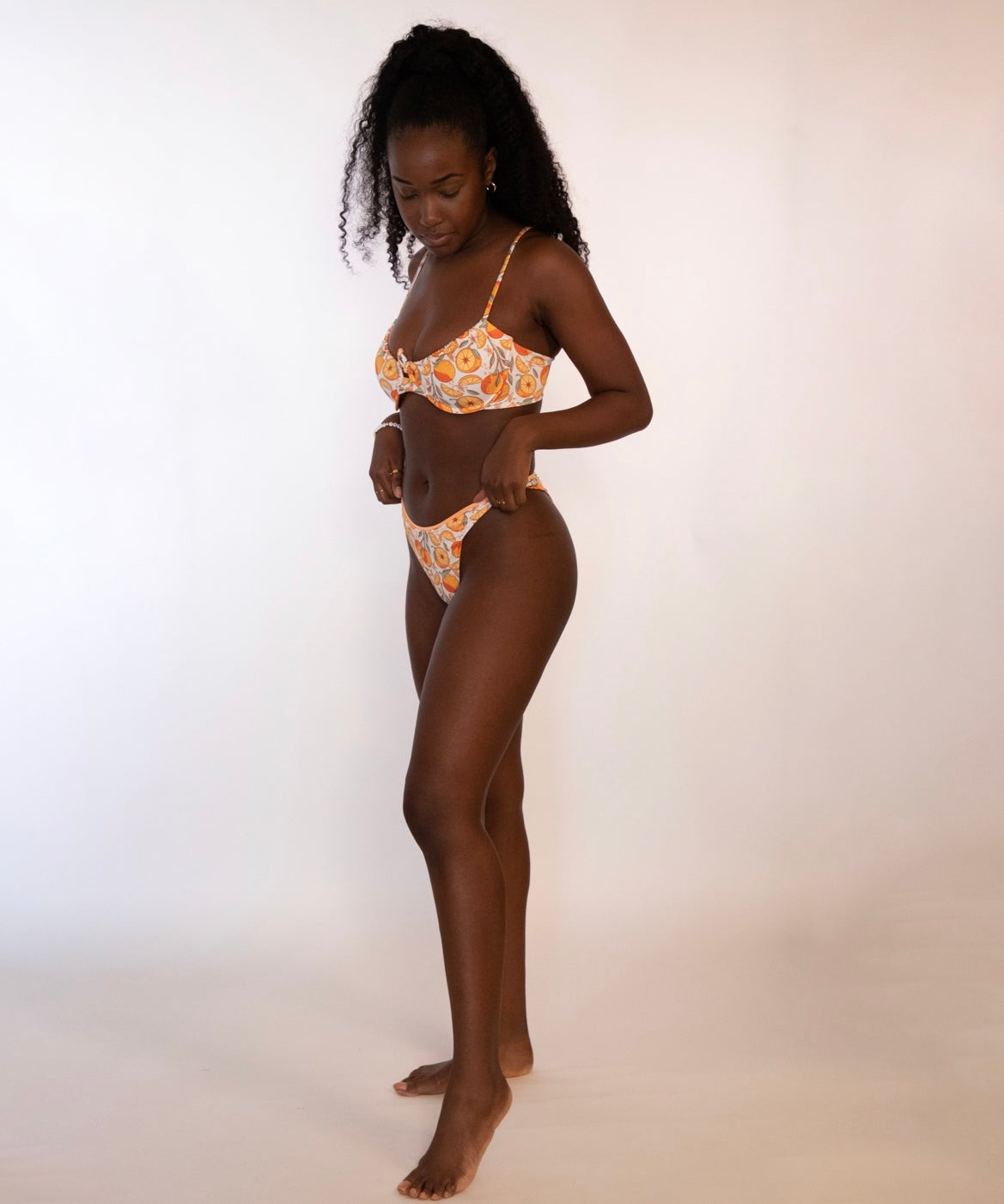 side view of woman wearing a reversible orange / orange print high hip thong bikini bottoms and matching underwire bikini top