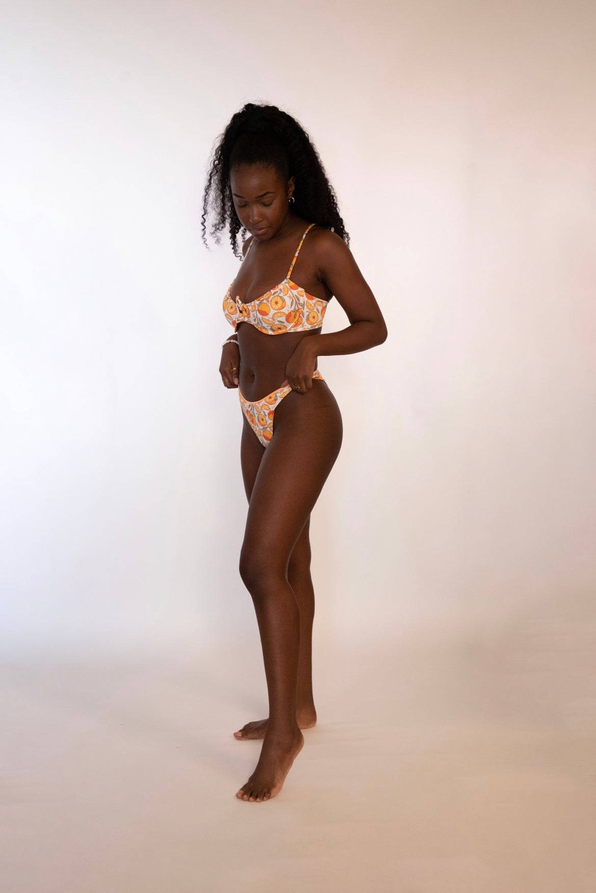 side view of woman wearing a reversible orange / orange print high hip thong bikini bottoms and matching underwire bikini top