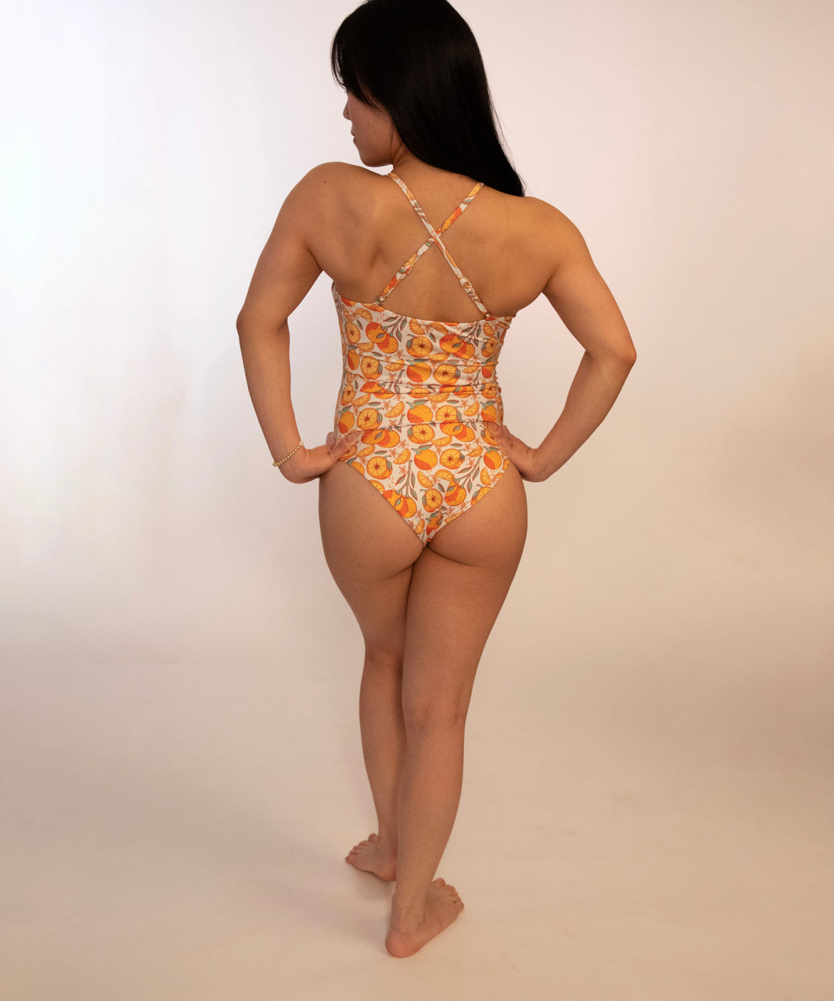 back of woman in reversible orange print one piece bathing suit with adjustable straps crossed into an x