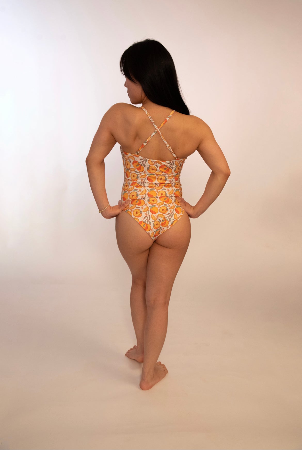 back of woman in reversible orange print one piece bathing suit with adjustable straps crossed into an x