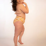 side view of curvy girl in orange print high waisted, high hip, reversible bikini bottoms and matching top