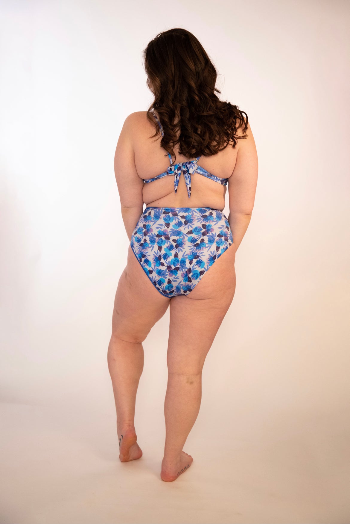 back view of plus sized woman in blue floral underwire bikini top and matching high waisted bottoms